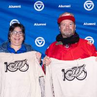 Couple standing in front of GVSU backdrop holding up their sweatshirts for the camera